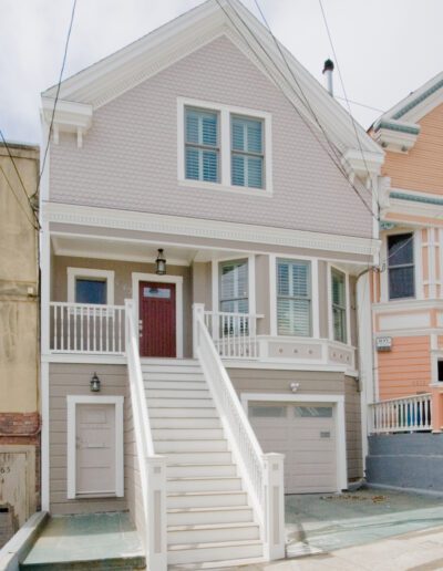 Two-story pink house with white trim, featuring a red front door and a garage underneath.