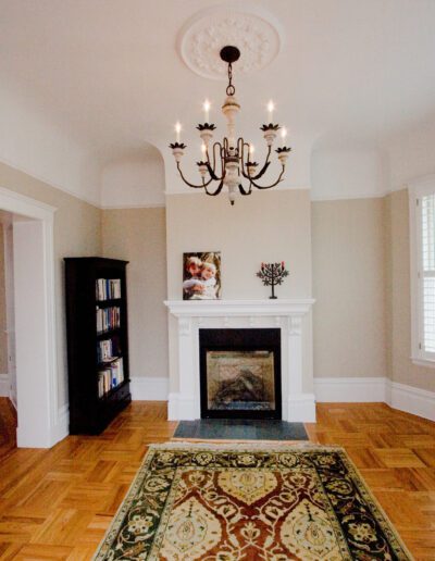 Elegant living room with a herringbone wood floor, decorative rug, white fireplace, and a traditional chandelier.