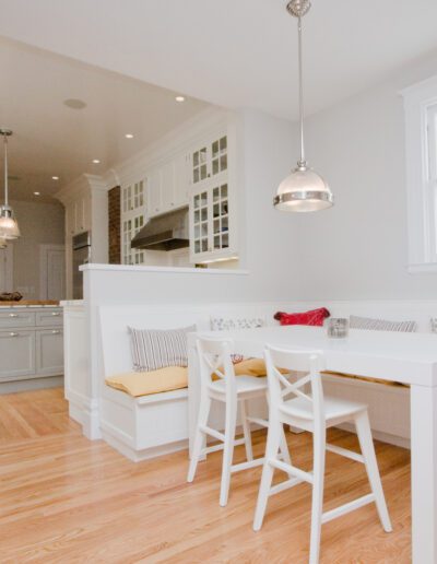 Bright and spacious kitchen interior with white cabinetry, hardwood floors, and a dining nook with bench seating.
